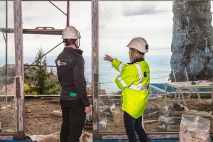 Deux experts Apave en casque de chantier observant l'extérieur depuis une baie vitrée en travaux