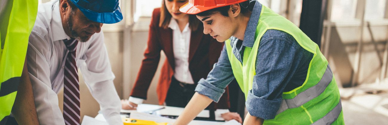 Équipe d'ingénieurs et d'architectes en réunion de chantier examinant des plans techniques.