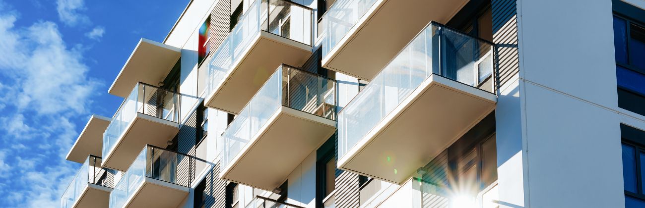 Façade d'un immeuble d'habitation moderne avec balcons vitrés sous un ciel bleu.