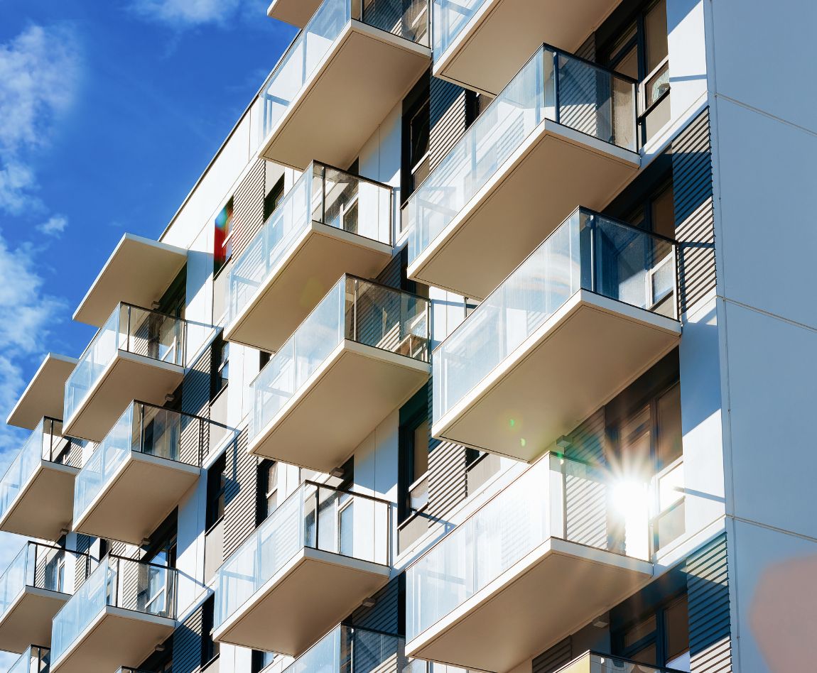 Façade d'un immeuble d'habitation moderne avec balcons vitrés sous un ciel bleu.