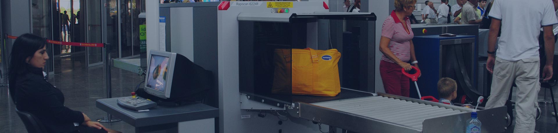 femme en train d'inspecter des bagages au niveau d'un portique de sécurité à l'aéroport