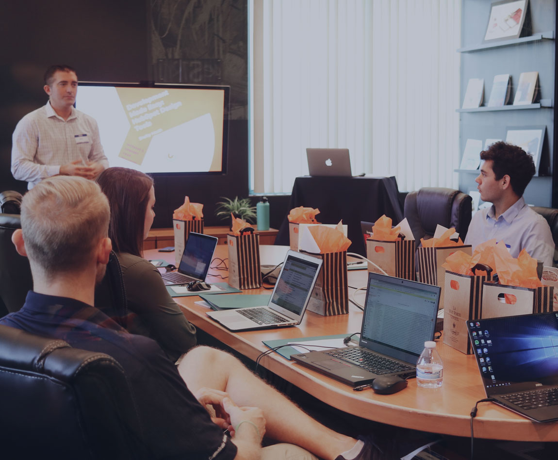 Un homme présente devant tout le monde autour d'une table devant leur ordinateur