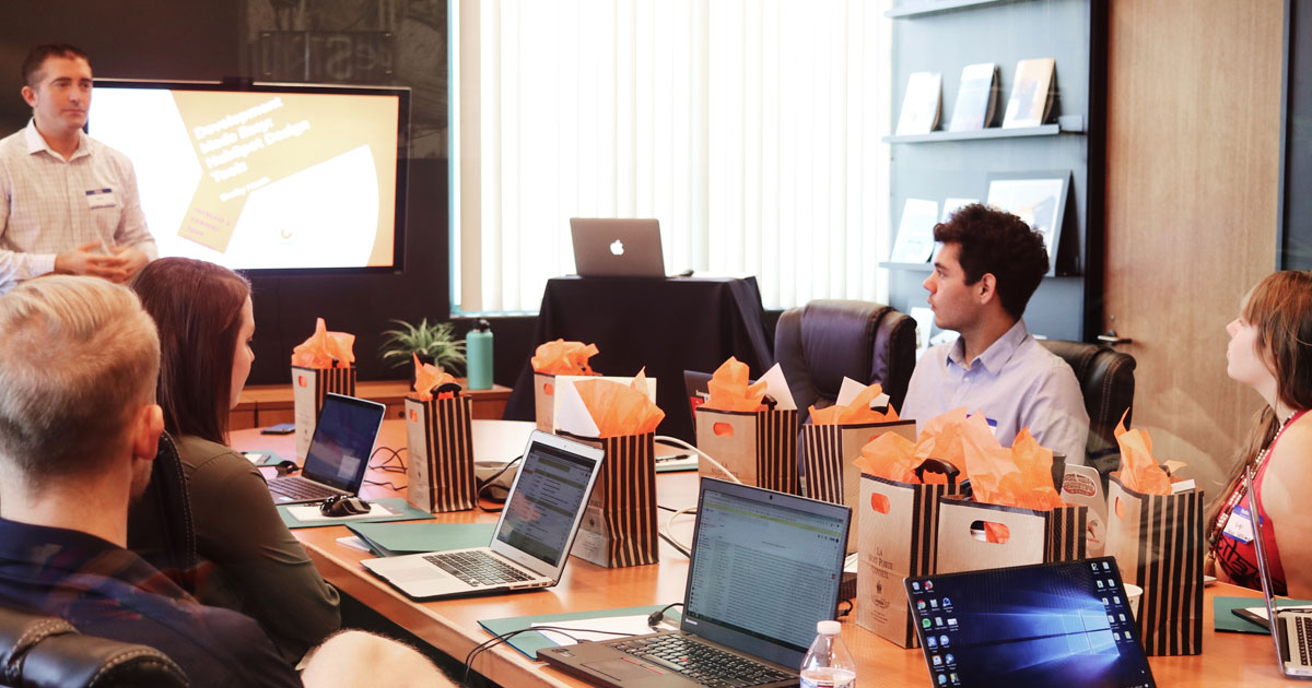 Un homme présente devant tout le monde autour d'une table devant leur ordinateur