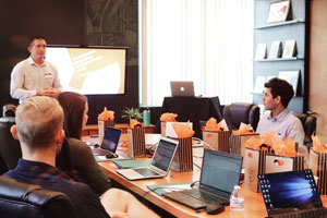 Un homme présente devant tout le monde autour d'une table devant leur ordinateur