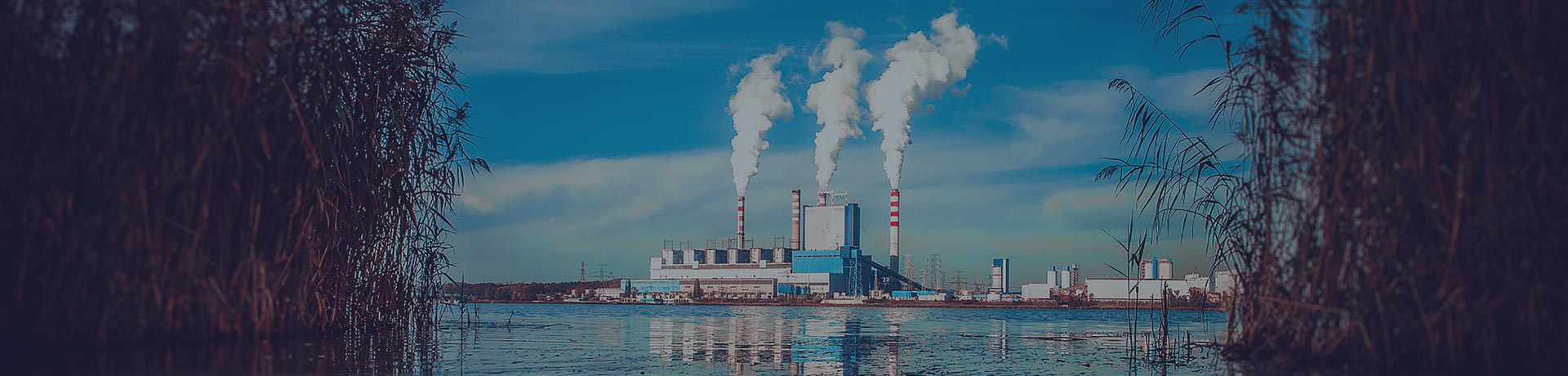 fábrica con 3 columnas de humo frente a un lago