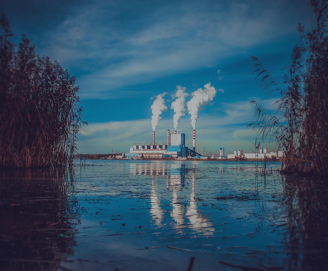fábrica con 3 columnas de humo frente a un lago