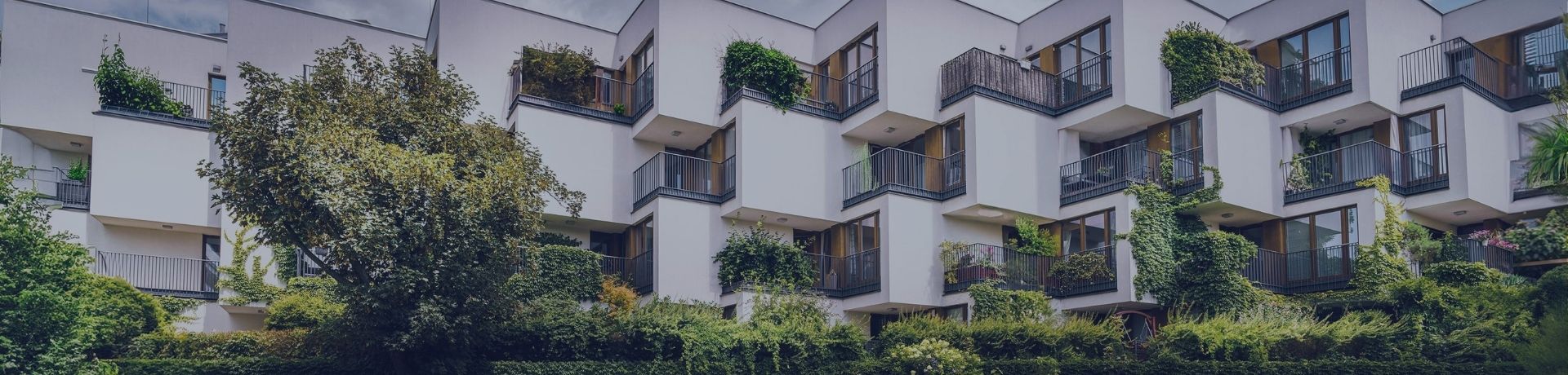 Immeuble résidentiel moderne blanc aux balcons végétalisés bordé par des jardins verdoyants.