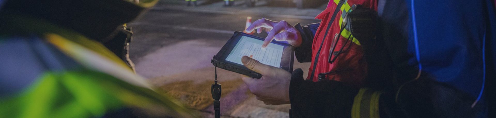 Pompiers en intervention de nuit utilisant une tablette pour la coordination des secours.