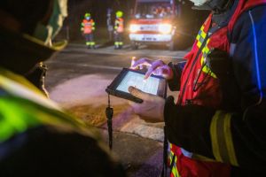 Pompiers en intervention de nuit utilisant une tablette pour la coordination des secours.