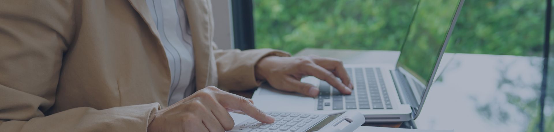 Personne utilisant une calculatrice et un ordinateur portable, avec des documents sur un bureau, symbolisant le calcul et la gestion financière ou environnementale.