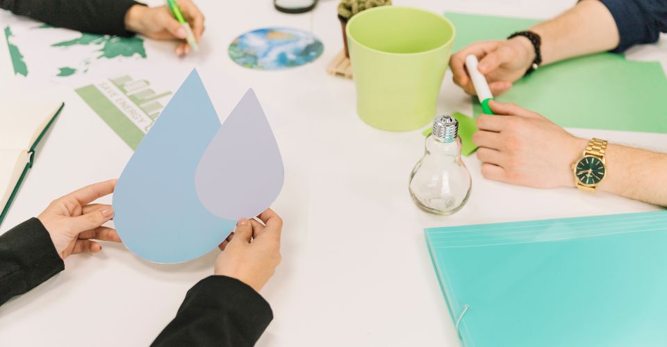 Mains tenant un symbole de goutte d'eau lors d'une réunion sur l'écologie avec des documents et plantes.