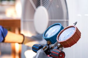 Technicien tenant un manifold de climatisation devant une unité extérieure de pompe à chaleur.
