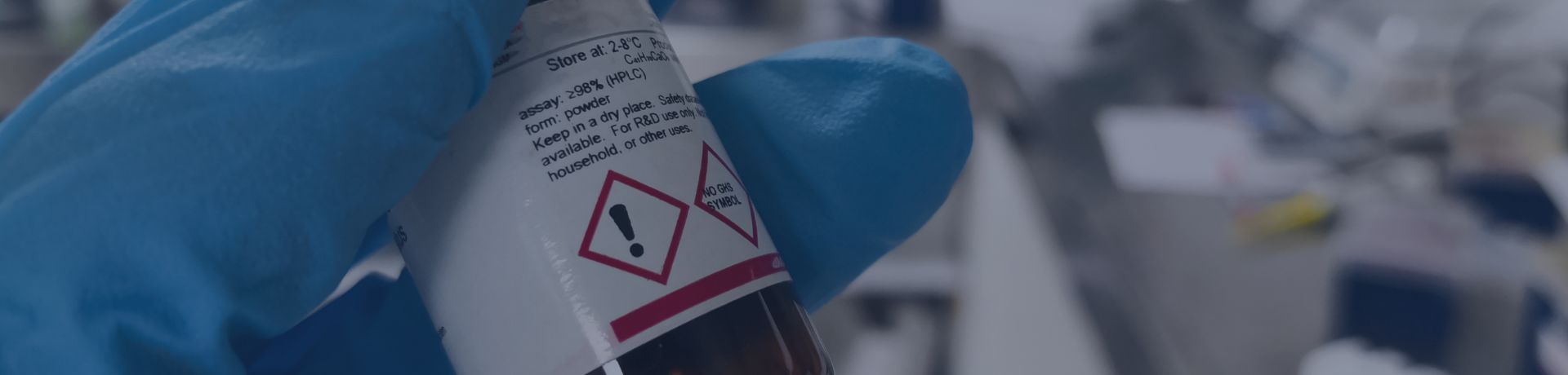 Main munie d'un gant de sécurité tenant un réactif chimique dangereux. Concept de recherche scientifique. Laboratoire avec différents équipements et matériels sur fond flou.