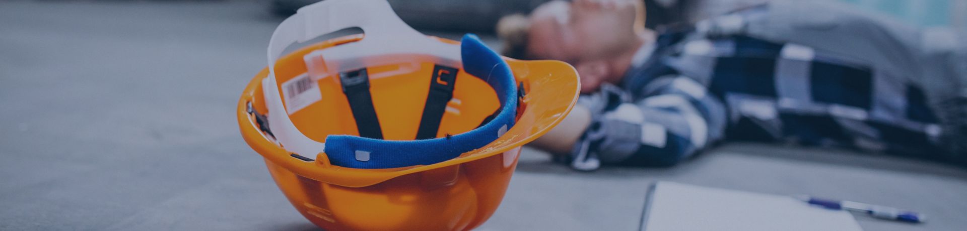 Travailleur blessé au sol dans un entrepôt, casque de sécurité à proximité.