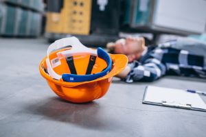 Travailleur blessé au sol dans un entrepôt, casque de sécurité à proximité.