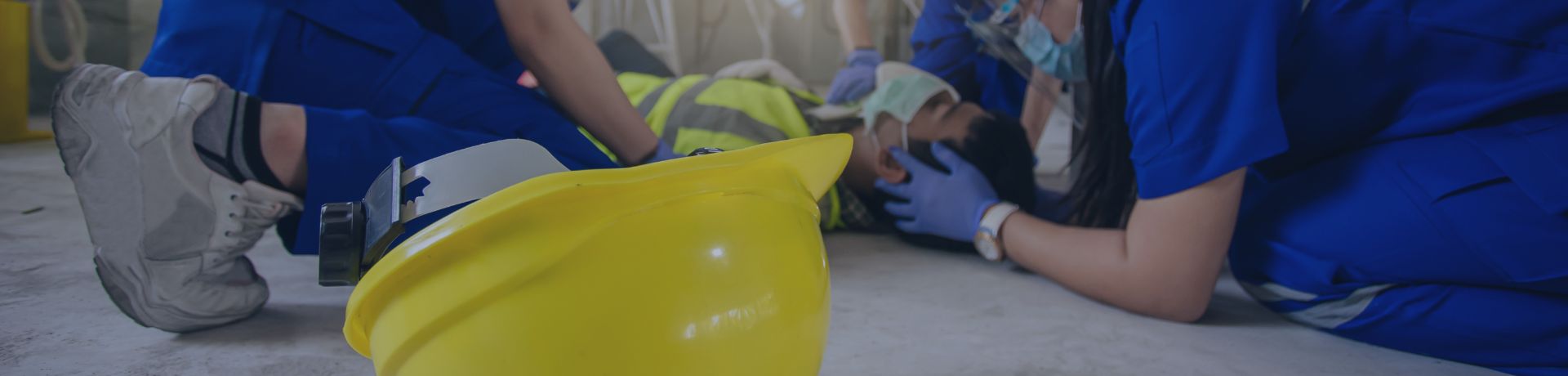 Secouristes en action autour d'un ouvrier blessé sur un chantier, casque de sécurité jaune au premier plan.