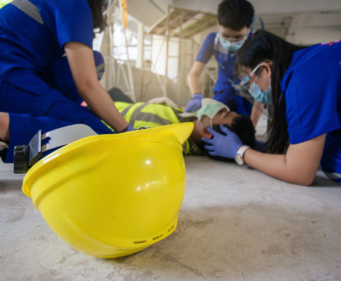 Secouristes en action autour d'un ouvrier blessé sur un chantier, casque de sécurité jaune au premier plan.