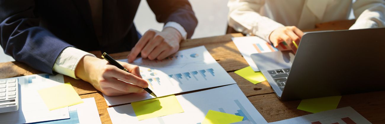 Deux personnes en réunion analysent des documents financiers et utilisent un ordinateur portable, illustrant la stratégie d'investissement et l'optimisation de la performance.