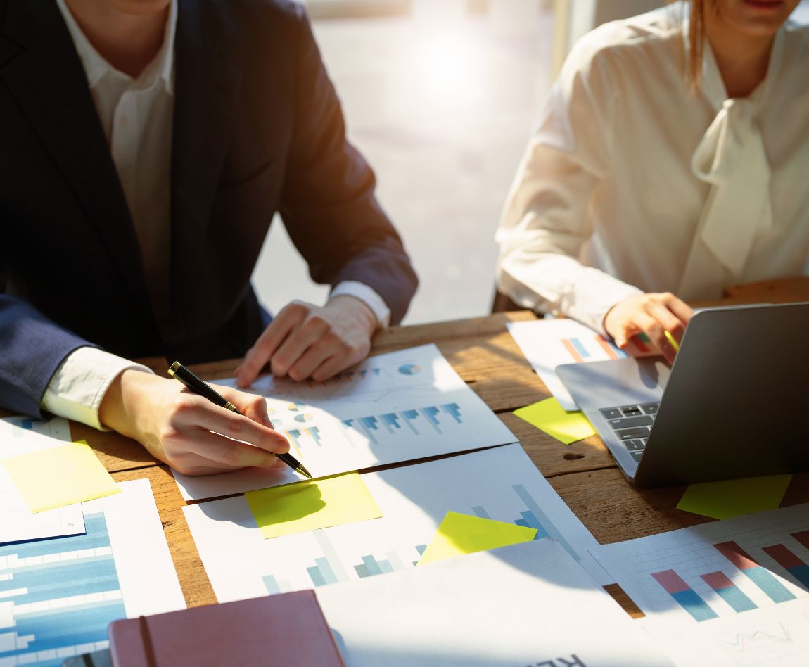 Deux personnes en réunion analysent des documents financiers et utilisent un ordinateur portable, illustrant la stratégie d'investissement et l'optimisation de la performance.