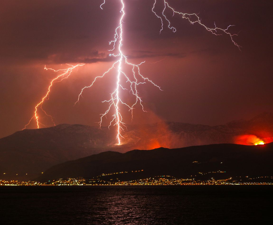 Éclairs frappant une montagne au-dessus d'une ville côtière illuminée de nuit.