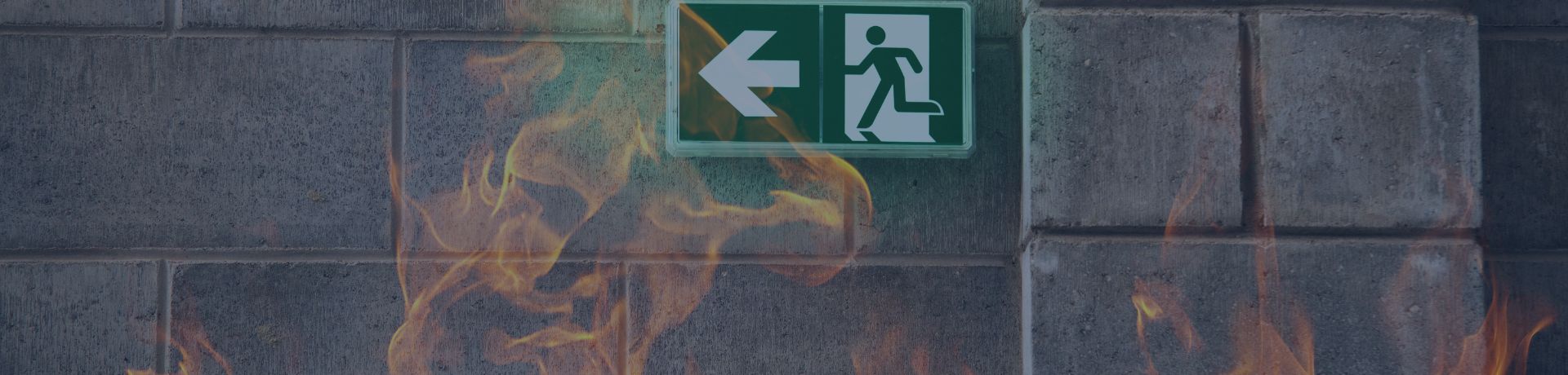 Panneau de sortie de secours lumineux sur un mur en pierre léché par des flammes.