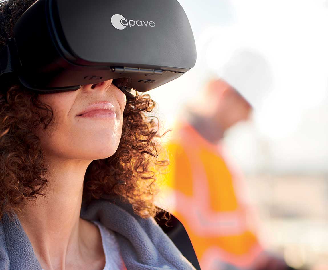 Une femme avec les cheveux bouclés porte un casque de réalité virtuelle avec le logo Apave