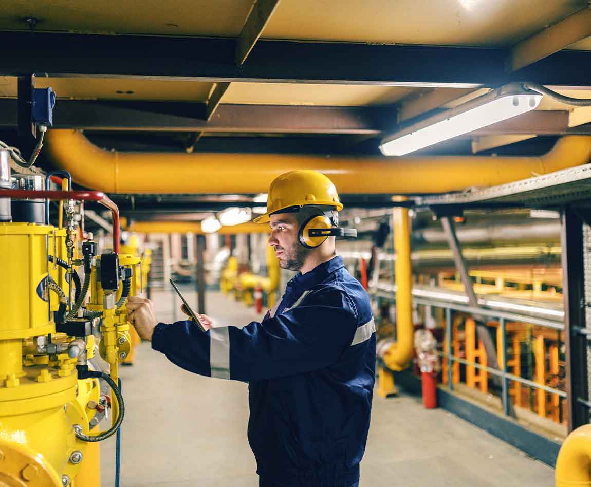 Jeune travailleur en tenue de protection à l'aide d'une tablette lors de la vérification des machines dans l'usine de chauffage.