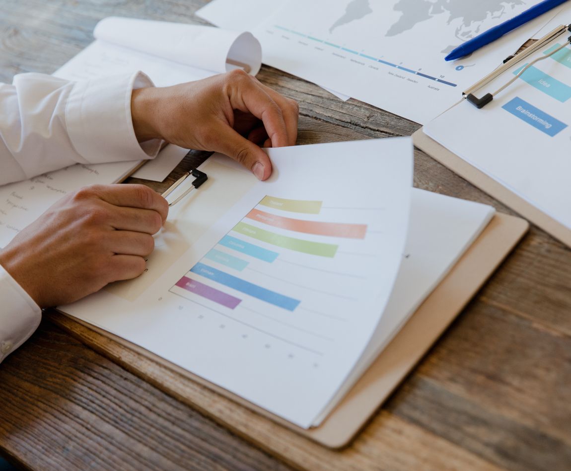 Gros plan sur des mains examinant un graphique à barres en couleurs, posé sur un bureau en bois, illustrant une analyse de données.