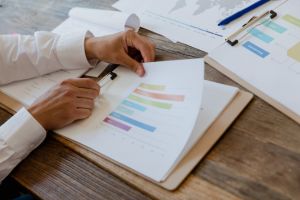 Gros plan sur des mains examinant un graphique à barres en couleurs, posé sur un bureau en bois, illustrant une analyse de données.