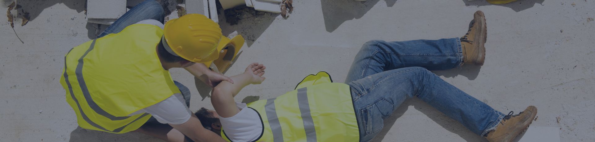 Vue en plongée d'un ouvrier blessé en gilet de sécurité jaune allongé au sol, secouru par un autre ouvrier.