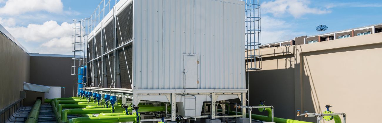 Des tuyaux verts connectés à une tour de refroidissement blanche sur un toit, illustrant un système de climatisation industriel.