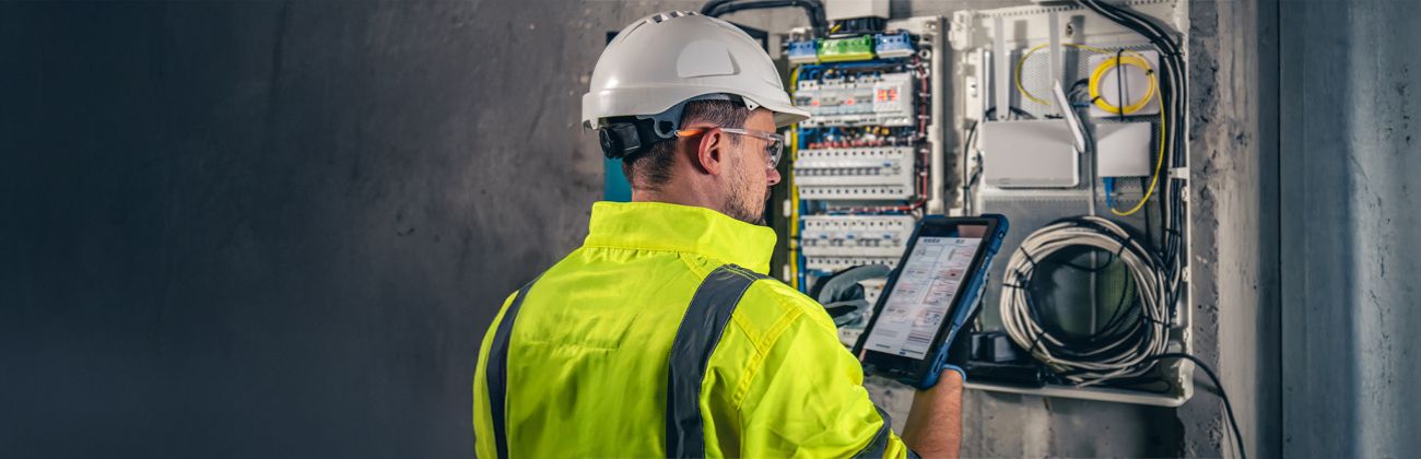 echnicien en électricité inspectant un tableau de distribution avec une tablette pour assurer la conformité et la sécurité.