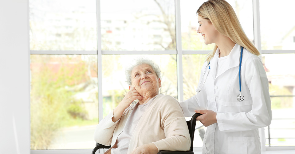 Une aide soignante en train de pousser une personne âgée qui est dans un fauteuil roulant