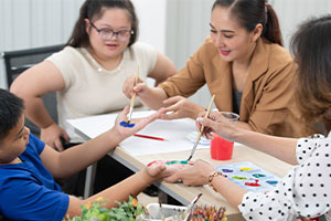Une dame aide des enfants handicapés, ils font de la peinture