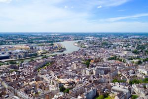 Vue aérienne panoramique d'une ville dense traversée par un fleuve sous un ciel bleu.
