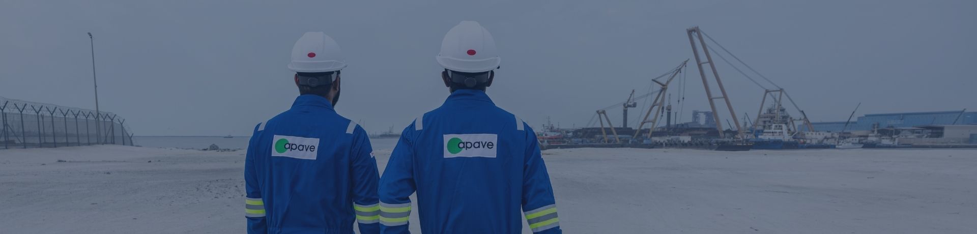 Two technicians in blue Apave jumpsuits walking from behind on an industrial site.