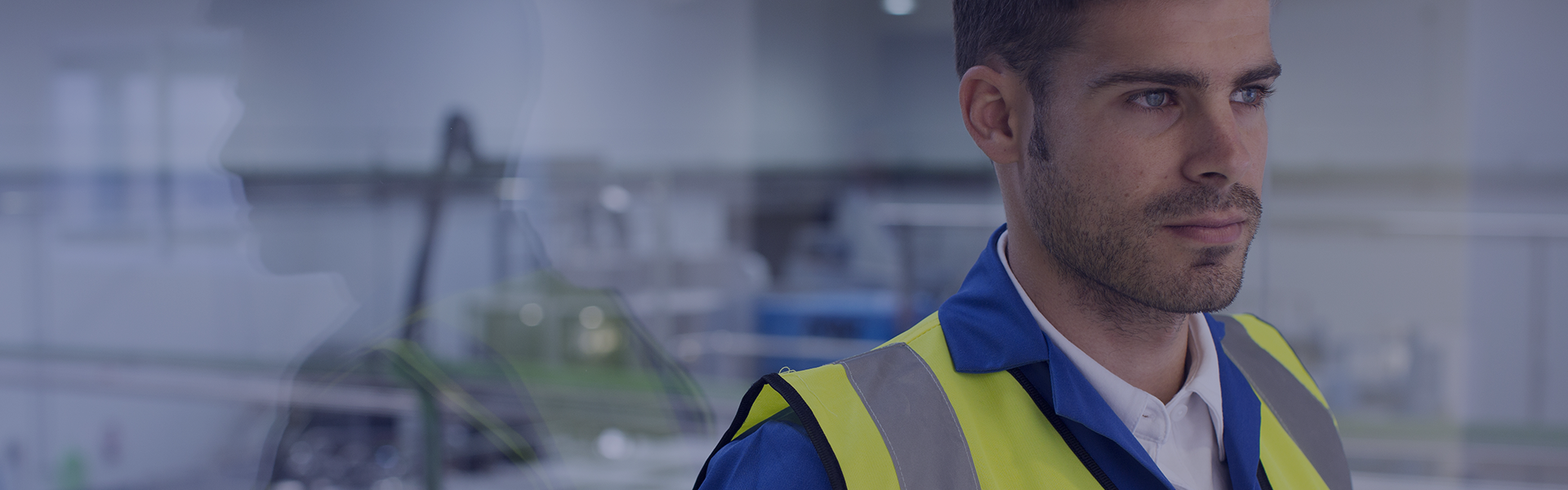Un homme regarde vers la droite. Il porte un bleu de travail et un gilet jaune.
