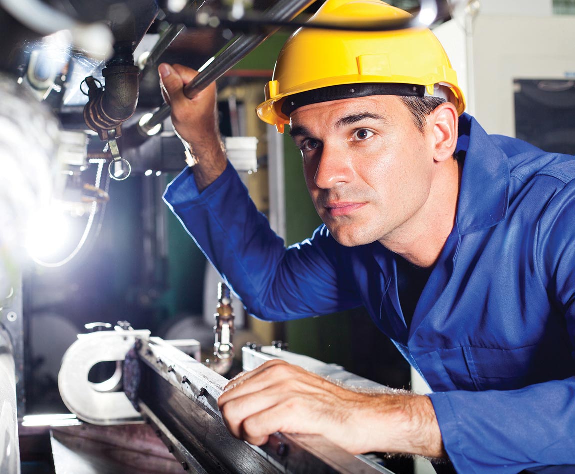 Un ouvrier de maintenance avec un casque de chantier jaune examine une machine industrielle.