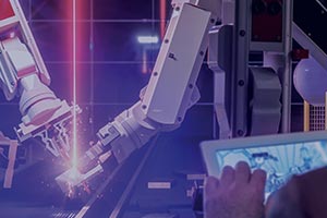 A man holds a tablet in front of robot arms working on a production line