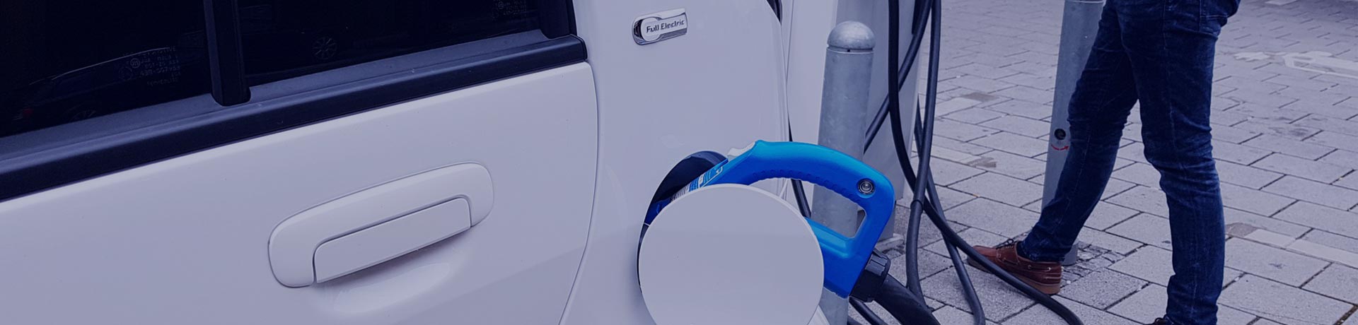 A man plugging his white electric car into a charging station