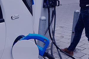 Un homme en train de brancher sa voiture électrique blanche sur une borne de recharge